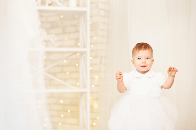 Retrato de una hermosa niña con un vestido blanco en el interior con adornos navideños