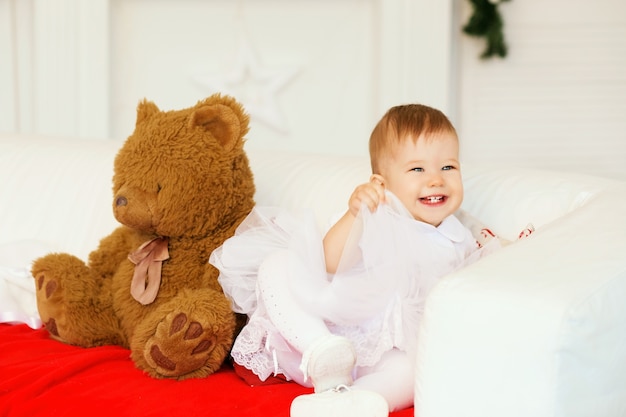 Retrato de una hermosa niña con un vestido blanco en el interior con un oso de peluche