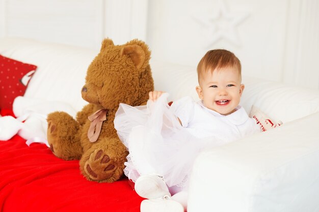 Retrato de una hermosa niña con un vestido blanco en el interior con un oso de peluche