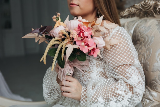 Foto retrato de una hermosa novia con un ramo de rosas hortensias y heces de color naranja pastel en sus manos en un interior claro