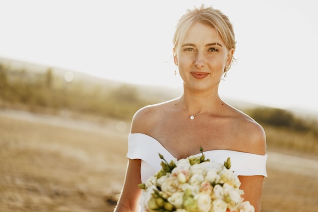 Retrato de una hermosa novia rubia con un vestido blanco con hombros descubiertos