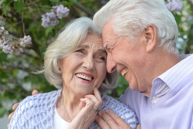 Retrato de una hermosa pareja de ancianos abrazándose con lilas en el parque