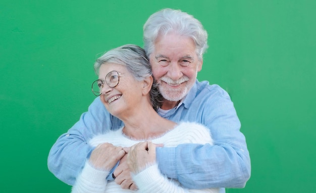 Retrato de una hermosa pareja de ancianos caucásica abrazándose con amor sonriendo de pie sobre fondo verde Pareja de ancianos expresando amor y ternura