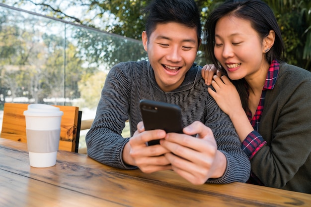 Retrato de hermosa pareja asiática mirando el teléfono móvil mientras está sentado y pasar tiempo en la cafetería.