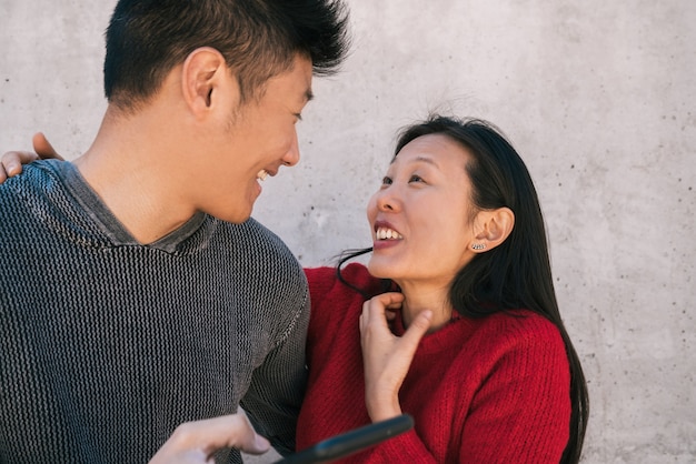 Retrato de hermosa pareja asiática mirando el teléfono móvil mientras pasan un buen rato juntos. Concepto de amor y tecnología.