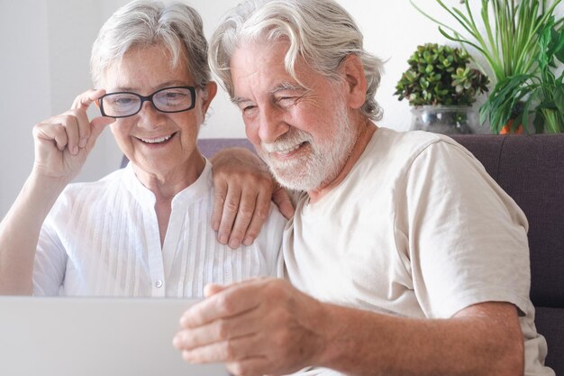 Retrato de hermosa pareja senior caucásica de abuelos con ordenador portátil en casa sonriendo