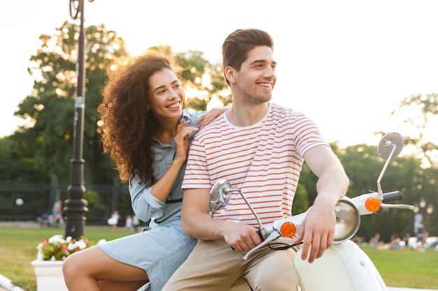 Retrato de hermosa pareja, sentados juntos en moto en el parque de la ciudad