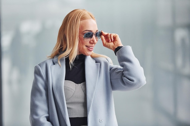 Retrato de una hermosa rubia con ropa elegante que se encuentra en el interior contra un fondo gris