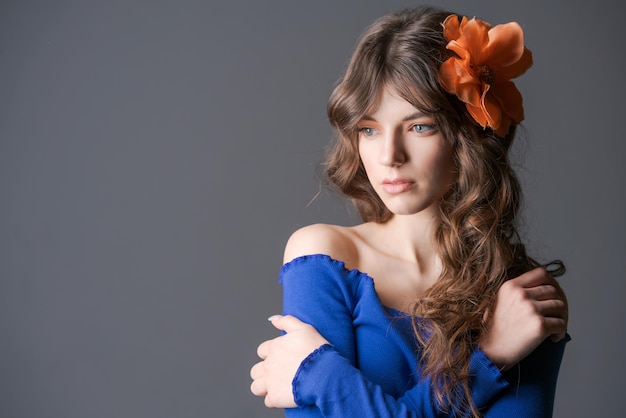 Retrato hermosa y tierna niña con flor en el pelo posando en un azul