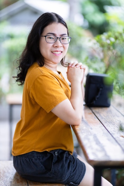 Un retrato de una hermosa viajera asiática feliz con un vestido amarillo anaranjado con un elegante estilo de vida hipster en la calle al aire libre en el día de verano en el parque o en el fondo de una cafetería sentada