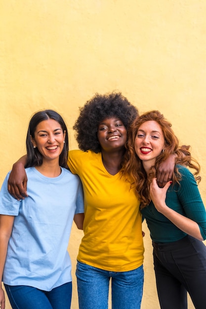 Retrato de hermosas amigas multiétnicas sonriendo en una pared amarilla divirtiéndose copiando y pegando