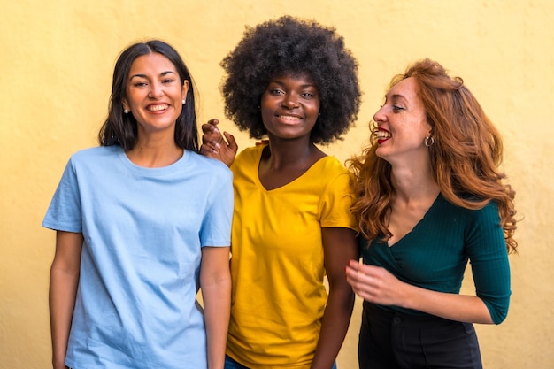 Retrato de hermosas amigas multiétnicas sonriendo en una pared amarilla