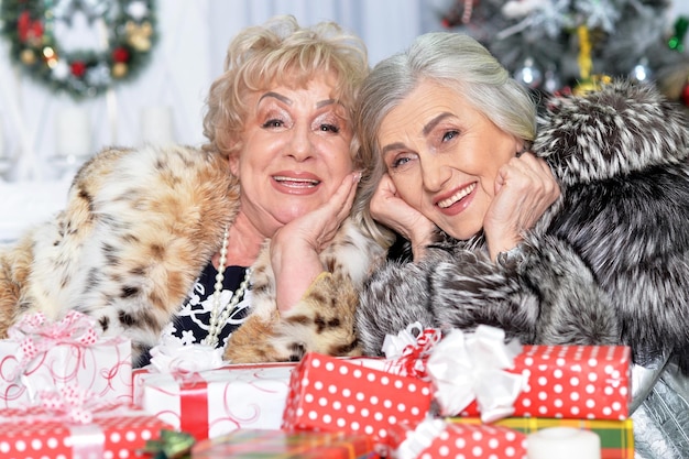 Retrato de hermosas mujeres mayores sentadas a la mesa con regalos de Navidad