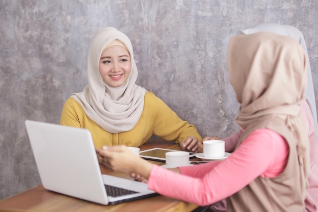 Retrato de hermosas mujeres musulmanas explicando el proyecto en la computadora portátil a su pareja en la cafetería.