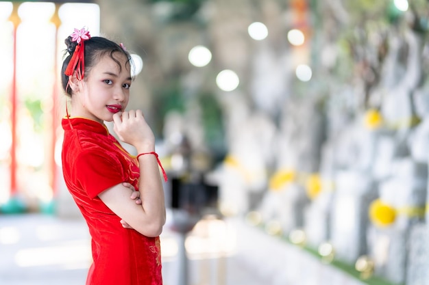 Retrato hermosas sonrisas Linda niña asiática con decoración de cheongsam chino tradicional rojo para el Festival de Año Nuevo Chino en el santuario chino