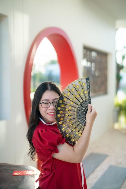 Retrato hermosas sonrisas mujer joven asiática vestida con decoración china tradicional roja y sosteniendo un Fanning chino para el Festival de Año Nuevo Chino en el café restaurante chino