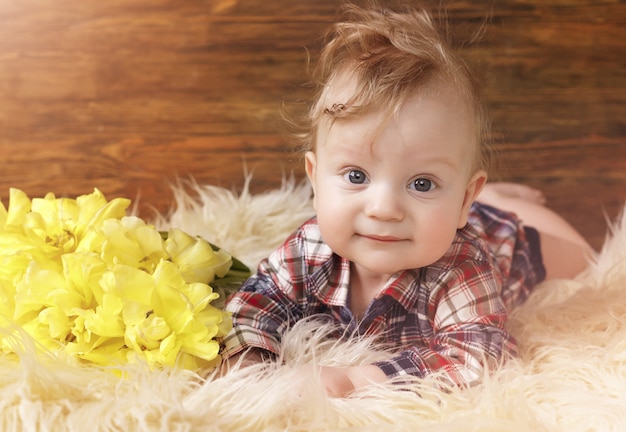 Retrato de un hermoso bebé que estaba acostado boca abajo cerca de tulipanes amarillos, ojos grandes.