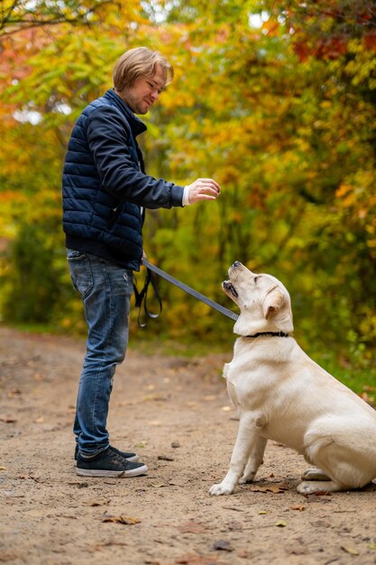 Retrato de un hermoso golden retriever sentado en el suelo. Retrato de cuerpo entero de un apuesto joven de pie en un parque.