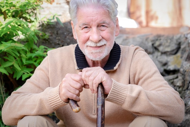 Retrato de un hermoso hombre mayor sentado al aire libre sosteniendo un bastón con un suéter de invierno, anciano sonriente mirando a la cámara