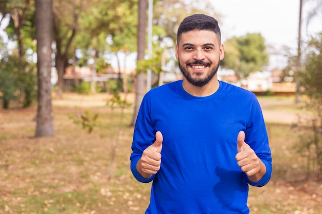 Retrato de un hermoso joven agricultor sonriente Hombre en la granja en un día de verano Actividad de jardinería Hombre brasileño Pulgares hacia arriba