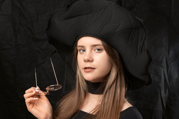 retrato, de, hermoso, mujer joven, en, sombrero negro, con, anteojos, en, ella, manos, estudio, retrato, de, dama, en, fondo negro