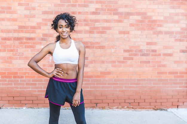 Retrato hermoso de la mujer negra contra la pared de ladrillo, estilo de la aptitud