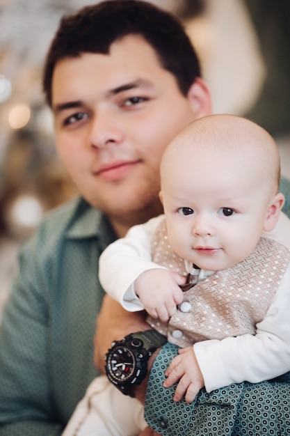 Retrato de hermoso papá caucásico se regocija con su pequeño y bonito niño en ambiente navideño