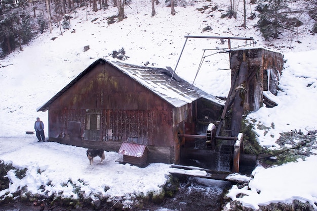 retrato de un herrero tradicional de confianza con un perro parado frente al antiguo molino de agua en invierno