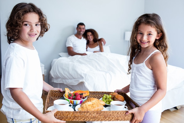 Retrato de hija e hijo llevando bandeja de desayuno para padres