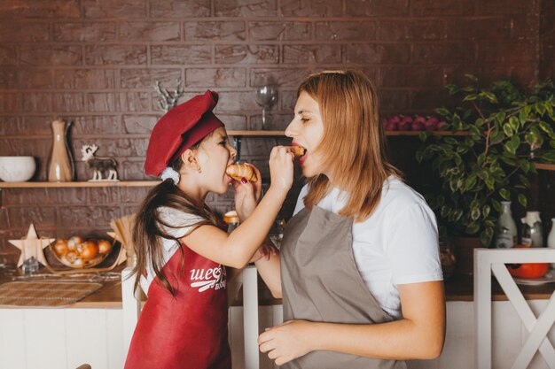 Retrato de hija y madre alimentándose con cupcakes en la cocina. día de la Madre