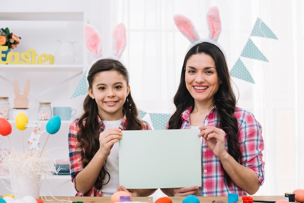 Foto retrato de hija y madre mostrando papel en blanco el día de pascua