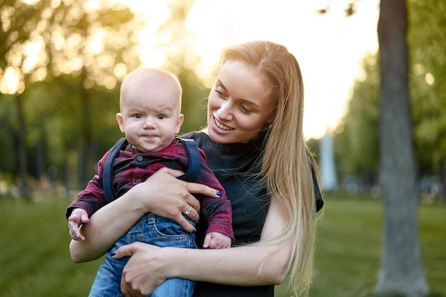 Retrato de un hijo lindo llevado por la madre en el parque al atardecer