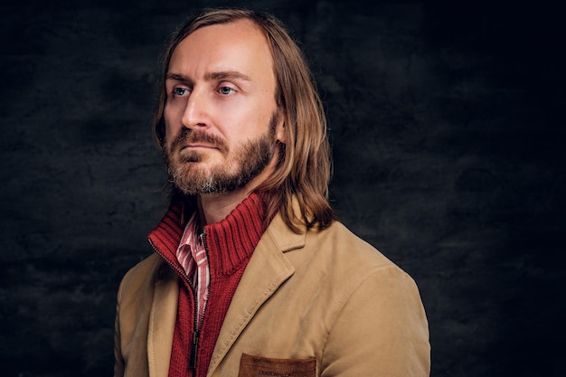 Retrato de hipster barbudo pensativo con chaqueta y suéter rojo en el fondo oscuro.