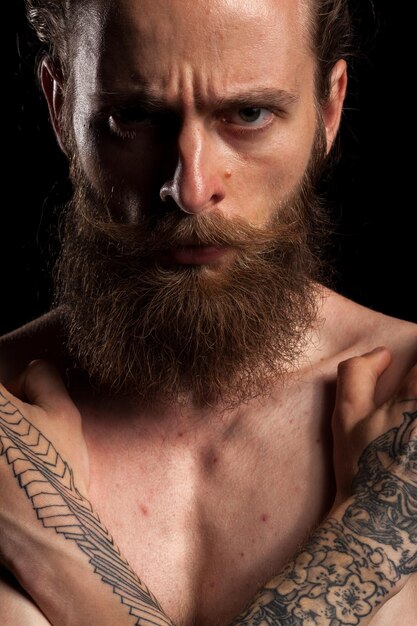 Retrato de un hipster barbudo tatuado de fondo negro en una foto de estudio. expresión y moda