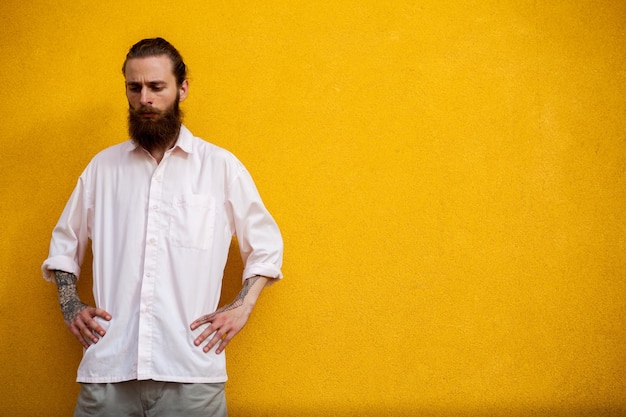 Retrato de hipster barbudo tatuado en pared amarilla posando al aire libre