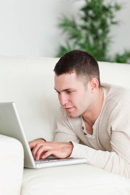 Retrato de un hombre acostado en un sofá usando una computadora portátil