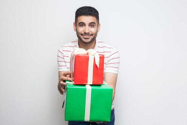 Retrato de hombre adulto joven guapo con barba en camiseta blanca de pie y sosteniendo dos caja presente, mirando a la cámara. Foto de estudio, fondo blanco, aislado, interior, espacio de copia