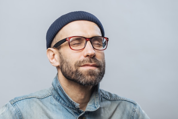 Retrato de hombre sin afeitar relajado con los ojos cerrados usa gafas, mantiene los ojos cerrados