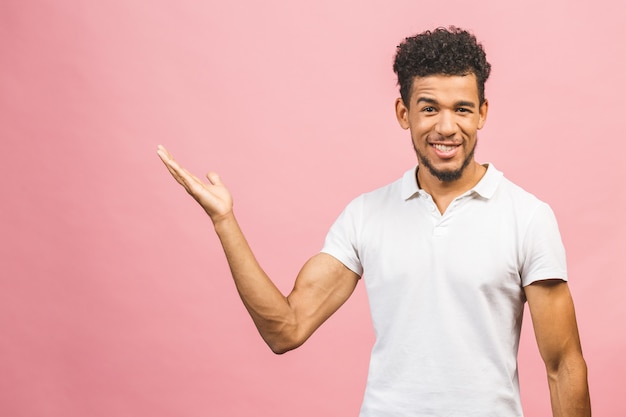 Retrato de un hombre africano feliz sonriente en señalar casual con los dedos a un lado aislado sobre fondo rosa.