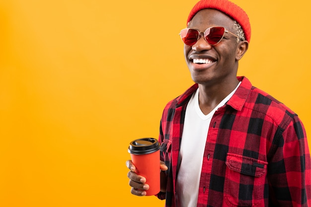 Retrato de un hombre africano negro vestido elegantemente sosteniendo un vaso de bebida sobre un fondo amarillo