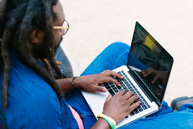 Retrato de hombre africano sentado afuera con laptop. Concepto de trabajo urbano