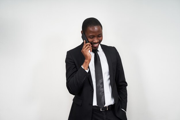 Retrato de hombre africano sonriendo mientras habla por teléfono con pared gris