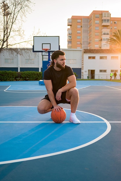 Retrato de un hombre afro latino posando con una pelota en una cancha de baloncesto