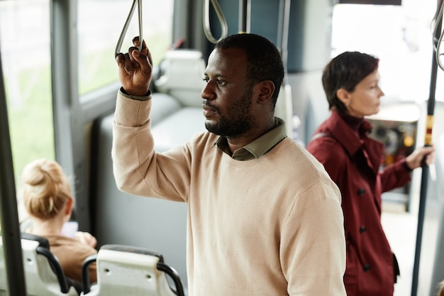 Retrato de hombre afroamericano adulto aferrándose a la baranda en el autobús mientras viaja en transporte público en la ciudad, espacio de copia