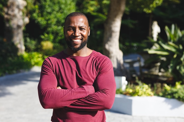 Retrato de un hombre afroamericano con los brazos cruzados sonriendo y mirando la cámara en un jardín soleado. pasar tiempo solo en casa.