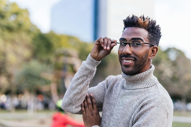 Retrato de un hombre afroamericano con chaleco de cuello alto sosteniendo sus gafas con la mano