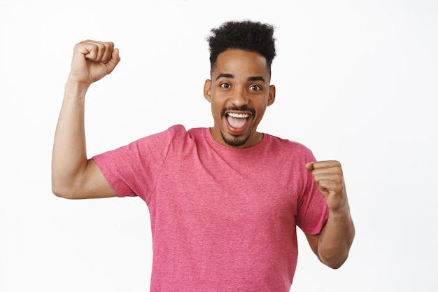 Retrato de un hombre afroamericano emocionado cantando, animando a los fanáticos del deporte, animando al equipo, celebrando la victoria, triunfando en la puntuación, de pie contra el fondo blanco