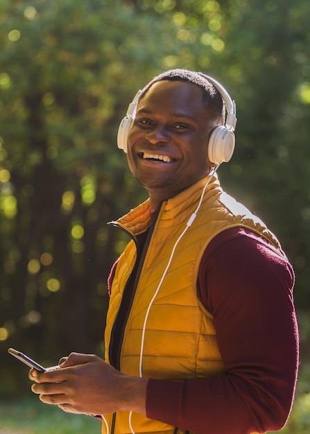 Retrato hombre afroamericano escucha música en el fondo del parque otoño Aplicación Gadget y concepto de servicio de transmisión