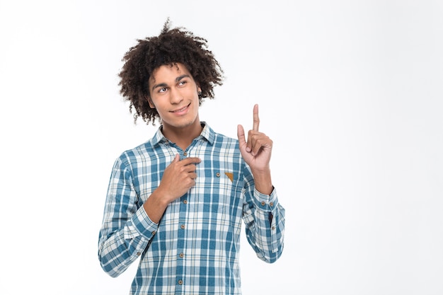 Retrato de un hombre afroamericano feliz apuntando con el dedo hacia arriba aislado en una pared blanca