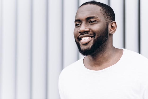 Retrato de hombre afroamericano guapo vistiendo ropa casual está mirando a cámara y sonriente